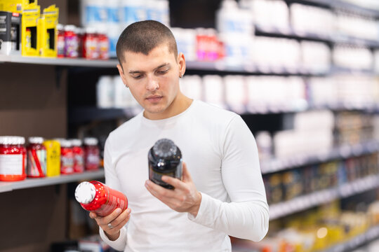 Focused young guy choosing a bottle of vitamin supplements in large sports nutrition store