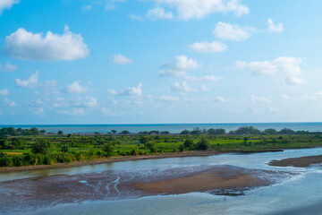 Coastal Landscape With River Estuary, Green Fields, And Blue Sky Over Calm Waters