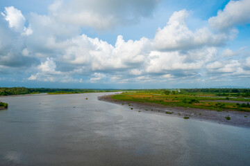A peaceful riverscape featuring a broad waterway, green riverbanks, and a dramatic cloud-filled sky.