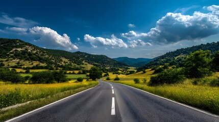 Naklejka premium Empty asphalt road curves through a lush green and yellow valley under a bright blue sky