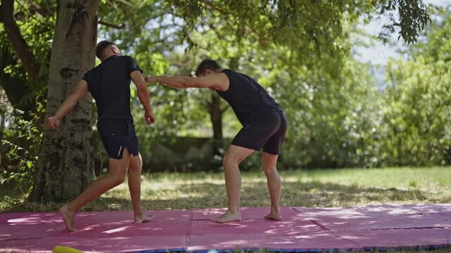 Active men are engaged in intense mixed martial arts training, practicing wrestling and grappling techniques on mats outdoors in a park. They are improving their combat skills.