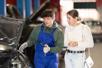 European woman in a car dealership tells the mechanic which parts of the car need to be checked. Mechanic gives recommendations to the woman about the car, oil change and engine condition