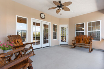 A porch with wooden chairs, a bench, and a ceiling fan