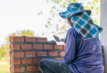 A construction worker, or mason, seen from the back, diligently lays a course of red bricks on a residential or commercial building site