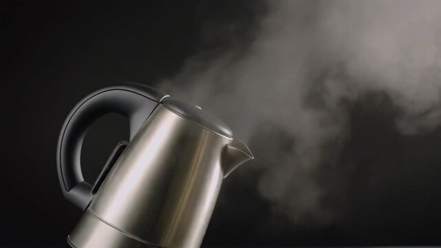 A modern stainless steel electric kettle boiling water and emitting steam against a dark background.