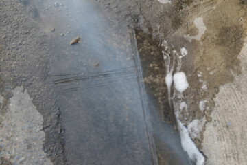 Water Puddle on Urban Street with Reflections and Foam in Industrial Area