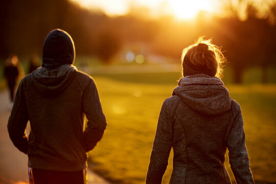 a man and woman walking in a park in golden light hour, seen from the back. - Powered by Adobe