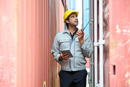 Warehouse worker using walkie-talkie to communicate during the work shift in the cargo containers area - Powered by Adobe
