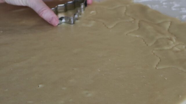 A close up shot of a Christmas tree shaped cookie cutter being used to cut out Christmas cookies from a sheet of cookie dough.