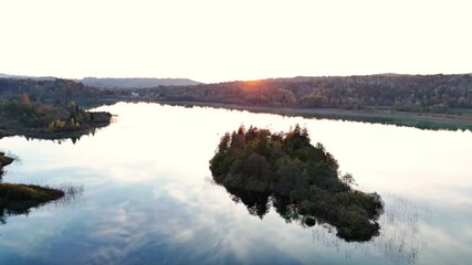 Aerial drone view of a small wooded island at sunrise on Lac d’Ilay in the Jura Mountains, Jura plateau in the background, near Le Frasnois and La Chaux‑du‑Dombief, Bourgogne‑Franche‑Comté, France