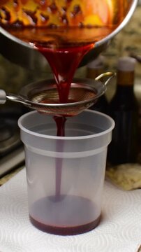 Close-up hot annatto-infused oil being poured through metal strainer. Red oil used in traditional Venezuelan dishes hallacas and bollitos. Preparation of natural oil extracted from onoto seeds.