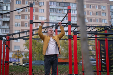 Man performs pull-ups in outdoor fitness area near residential buildings during early evening hours