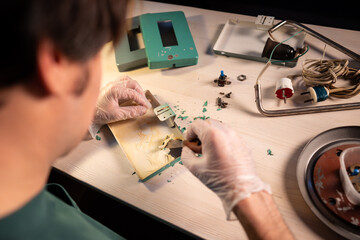 Man working at home workshop preparing parts of vintage lamp for repairing, using putty knife and...