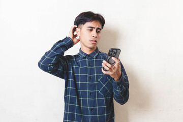 Frustrated young Asian man reacting to a smartphone problem, showing stress and discomfort while checking his phone. 