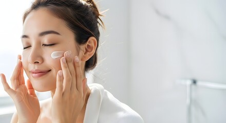 A radiant young girl is seen gently rubbing lotion on her cheeks as part of a glowing daily skincare beauty and self-care concept