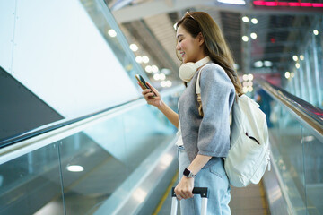 Young traveler on airport walkway using her phone with luggage and backpack.