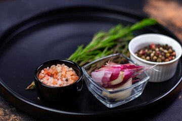 Colors of ingredients on a round black plate with various spices and herbs arranged for cooking or food preparation