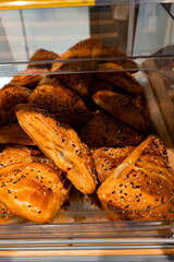 Freshly baked pastries in a display case at a local bakery during the morning rush hour, showing various shapes and textures with sesame seeds
