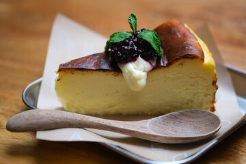 Creamy cheesecake slice topped with berry compote and mint leaves, served on parchment paper with a wooden spoon for a cozy dessert presentation. © Ahmad