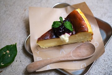 Creamy cheesecake slice topped with berry compote and mint leaves, served on parchment paper with a wooden spoon for a cozy dessert presentation. © Ahmad