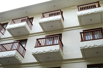 Exterior view of a multi-story apartment building featuring clean white walls, wooden rail balconies, and geometric decorative patterns.