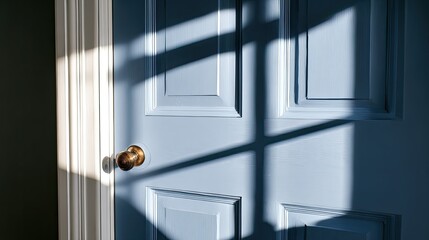 Sunlight casts sharp geometric shadows across a pale blue paneled interior door with a brass knob