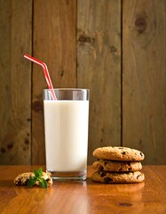 Glass of milk with cookies and a straw, set against a wood backdrop