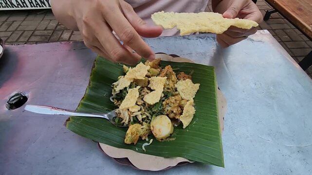Enjoying traditional Indonesian pecel with crispy toppings. Taste the rich flavors of pecel with crunchy crackers and sauce. Savoring the delicious pecel dish, served with crispy crackers