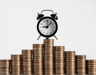 An alarm clock sits atop the highest stack of coins, part of a rising and falling coin graph, against a clean white background.
