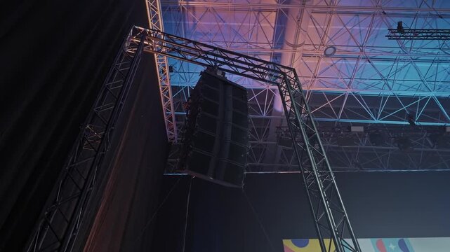 towering speaker stack hanging from metal truss under blue lit event ceiling
