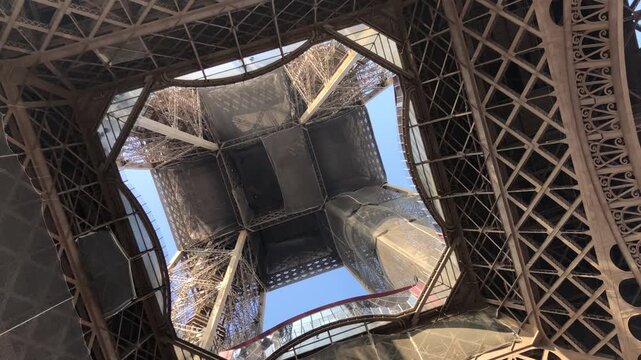 Rotating upward shot from beneath the Eiffel Tower, revealing its steel lattice structure against a clear sky and creating a dynamic architectural perspective.