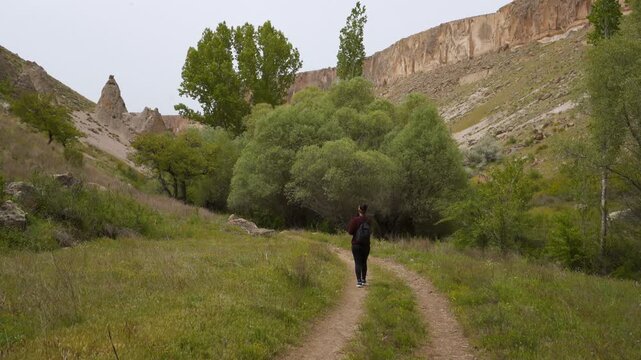 Solo woman traveler walking on a dirt path through the green Soganli Canyon landscape in Turkey