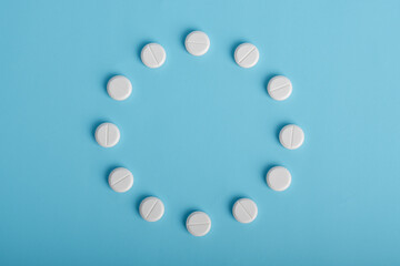 White pills arranged in a circle on a blue background, top view with space for text. Drug dosage...