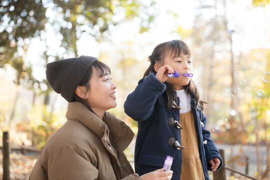A young mother and her adorable daughter playing with soap bubbles in an autumn park - Powered by Adobe