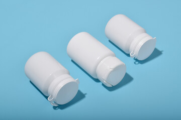 Three white medicine bottles on blue background, concept of pharmacy, healthcare products and medical supplies.