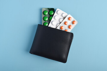Wallet with a blister pack of pills on a blue background, top view. Concept of health care costs, medical expenses, and financial responsibility in medicine.