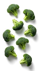 Fresh green broccoli florets scattered on a white background with strong shadows