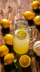 A rustic glass mug of fresh lemonade surrounded by yellow lemons and a garlic bulb on a dark wooden table. A natural, healthy composition for wellness and detox concepts.