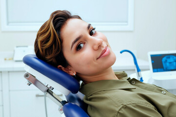 Portrait of young adult Hispanic woman reclining in dental chair smiling at camera during dental appointment in modern clinic with dental equipment visible in background