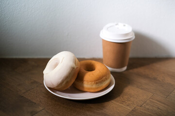 Breakfast donut in white plate and hot coffee on wooden table.