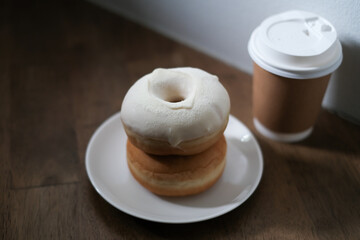 Breakfast donut in white plate and hot coffee on wooden table.