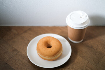 Breakfast donut in white plate and hot coffee on wooden table.