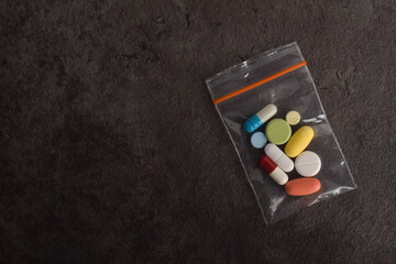 Mixed medical pills inside a small plastic zip bag on dark textured background, top view, concept of medicine, therapy and pharmacy.