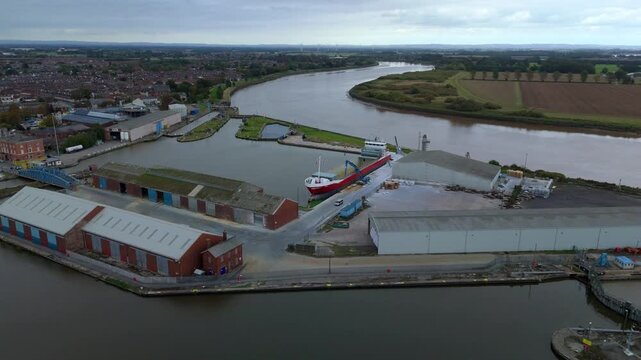 Dynamic drone approach over Goole harbour showing active shipping operations, industrial cranes, bulk handling equipment, and wide-spanning port warehouses.