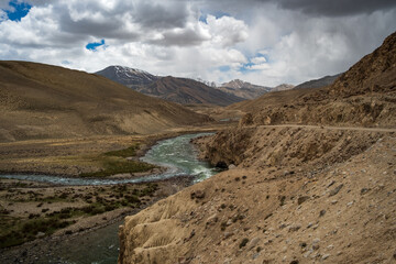 The Panj River snakes through the narrow Wakhan Corridor, creating the geographical border between Tajikistan and Afghanistan. Dramatic mountain river valley view from the Pamir Highway