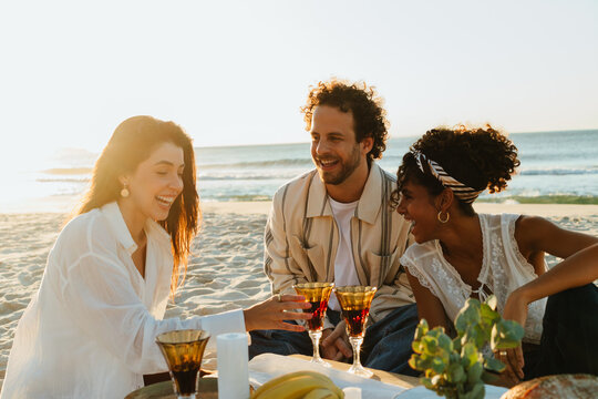 Friends having a sunset beach picnic with drinks