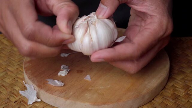 Hands Peeling Fresh Garlic Bulb on Cutting Board