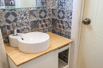 Bathroom vanity with wooden countertop, white ceramic vessel sink, patterned tile wall, clean...