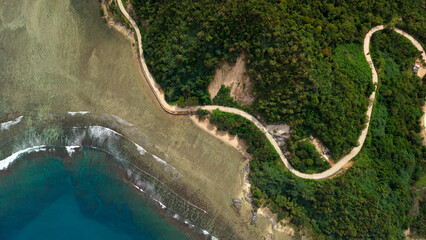 Vertical top-down drone shot of winding concrete coastal road hugging the shoreline next to turquoise coral reef in Barangay Cheey Busuanga Island Philippines