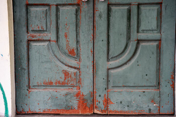 Weathered wooden doors with peeling paint in shades of teal and rust.